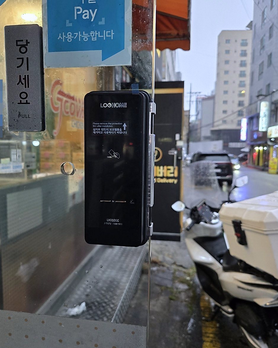 덕양구 원신동 출장 — 유리문에 붙은 검은 카드식 도어락과 문 위 당기세요 표지판, 문밖 젖은 길과 세워 둔 오토바이